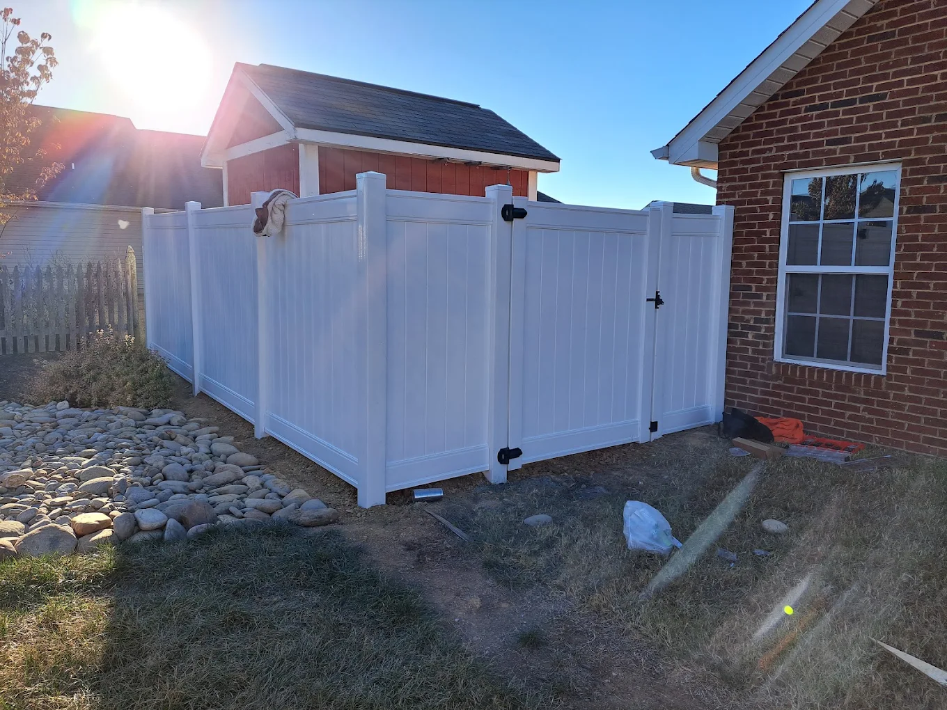 White vinyl privacy fence with gate installed in residential backyard next to brick house