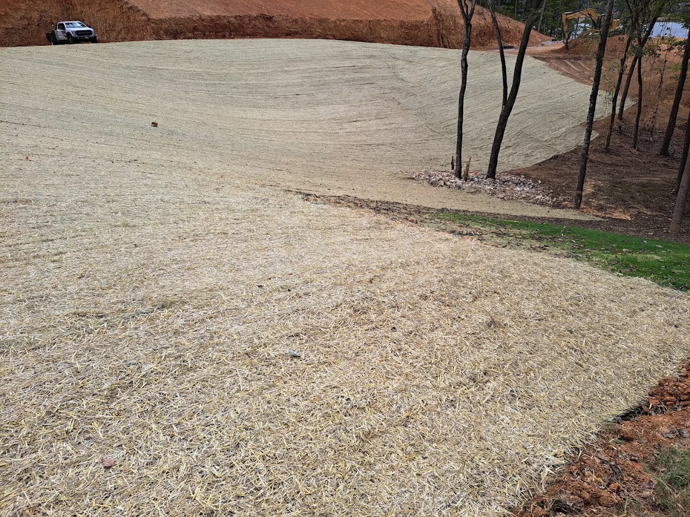 Erosion control site with straw matting, bare soil banks, trees, and work vehicle