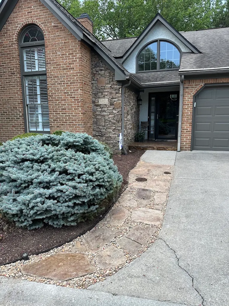 Brick home with stone entry, blue-gray evergreen shrub, and gray garage door
