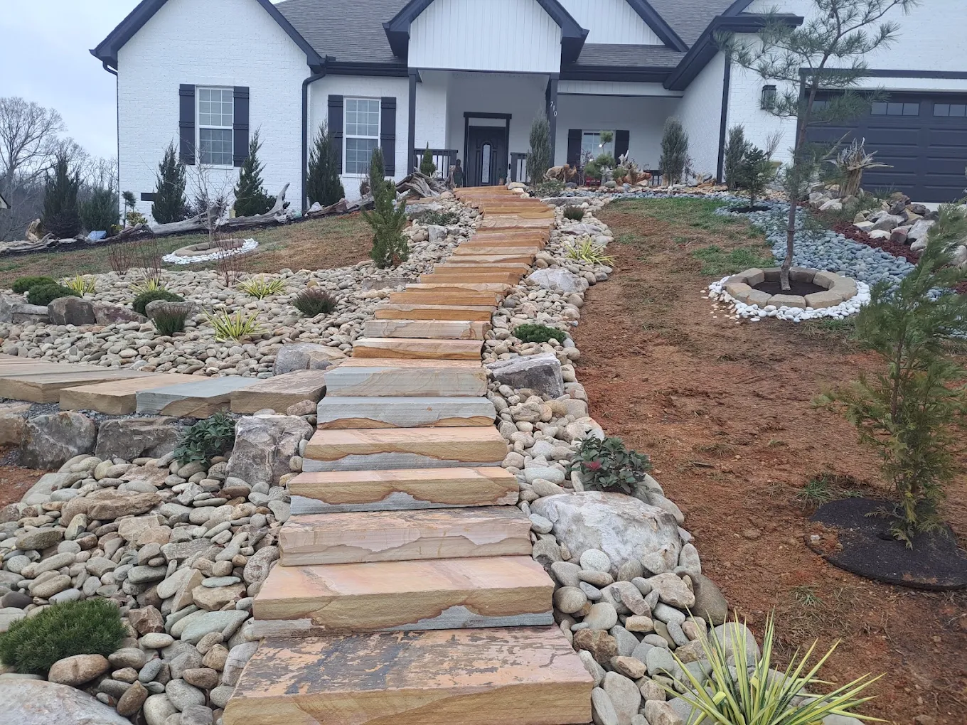 Modern home with stone pathway, landscaping rocks, fire pit, and newly planted shrubs in front yard