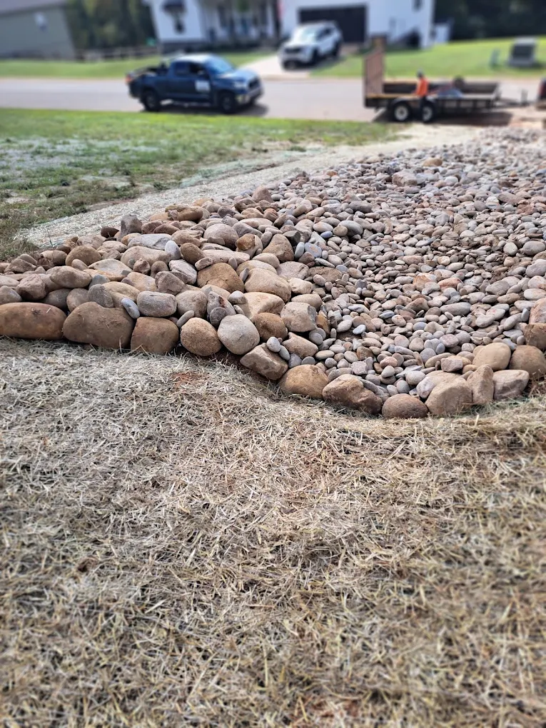 Gravel and stone materials arranged in rows along residential driveway with truck and vehicles in background