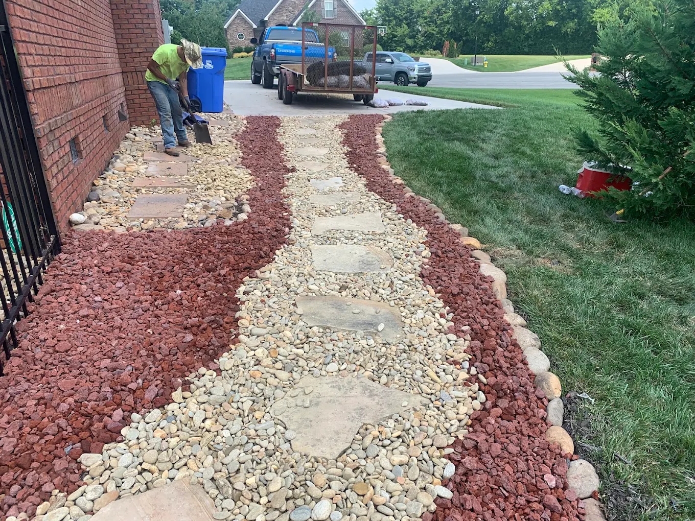 Worker installing decorative red and tan mulch landscaping border along brick home foundation