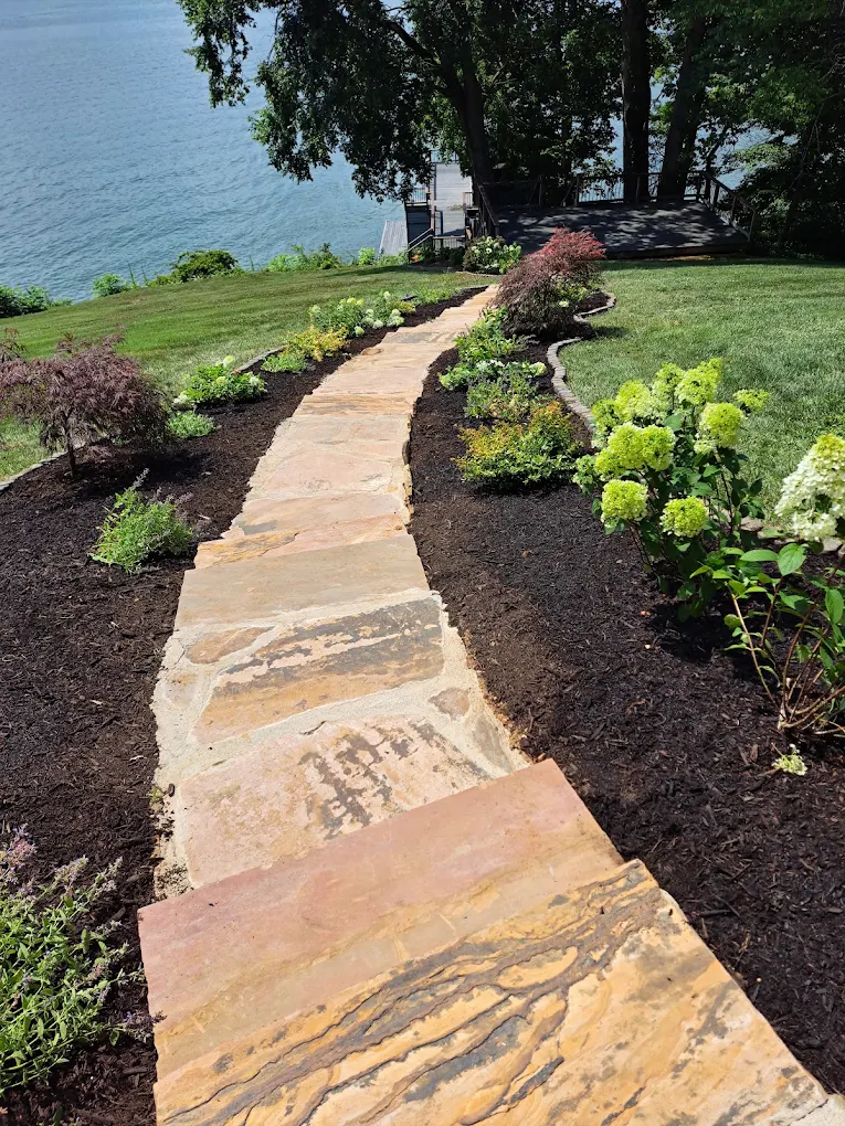 Stone pathway through landscaped garden with shrubs leading to waterfront deck