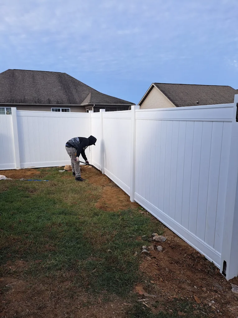 Worker installing white vinyl fence in residential backyard