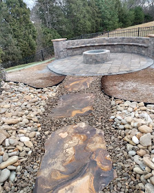 Curved stone fire pit with metal ring surrounded by river rocks and gravel pathway