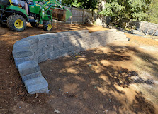 Curved stone retaining wall under construction in landscaped garden with machinery
