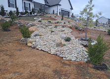Residential backyard with white river rock landscaping and sparse vegetation against brown soil