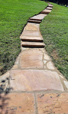 Stone pathway winding through green lawn with alternating light and dark colored pavers