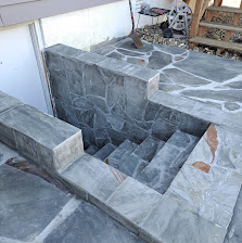 Stone staircase under construction with concrete steps and metal framing visible indoors