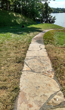 Stone pathway winding through green lawn toward water and trees