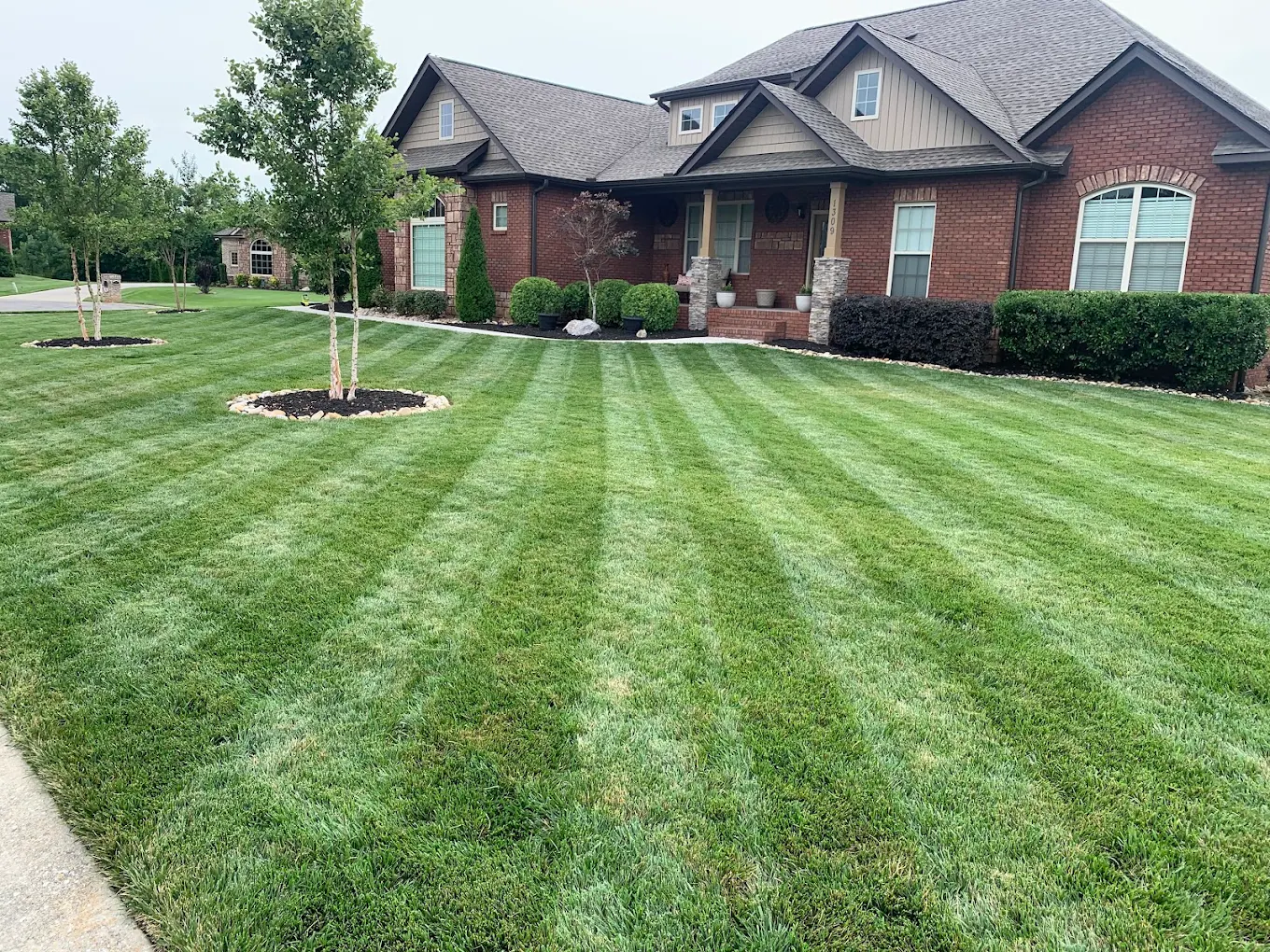 Well-maintained brick home with striped lawn, landscaped beds, and young trees