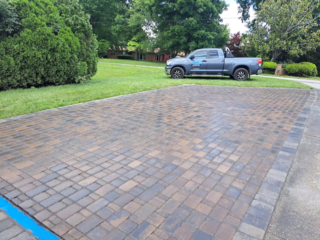 Brick paver driveway in herringbone pattern with blue pickup truck and manicured lawn