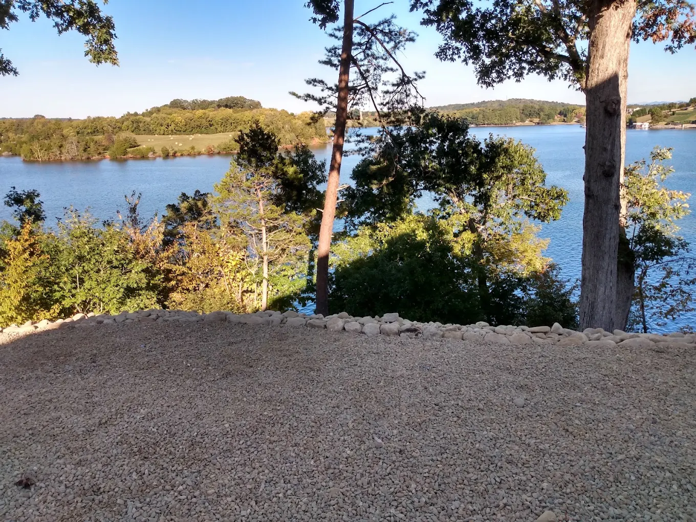 Scenic overlook with gravel patio, tall trees, and expansive blue lake surrounded by forested hills