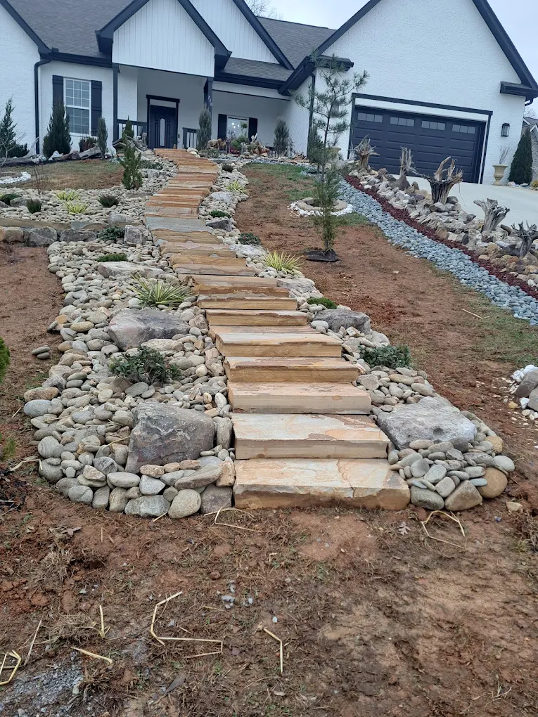 Wooden step pathway with river rock borders leading to modern white house with dark trim